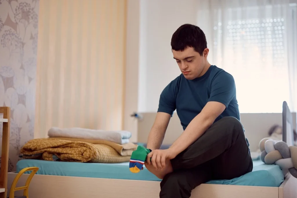 Disabled man sitting on the edge of his bed putting his socks on