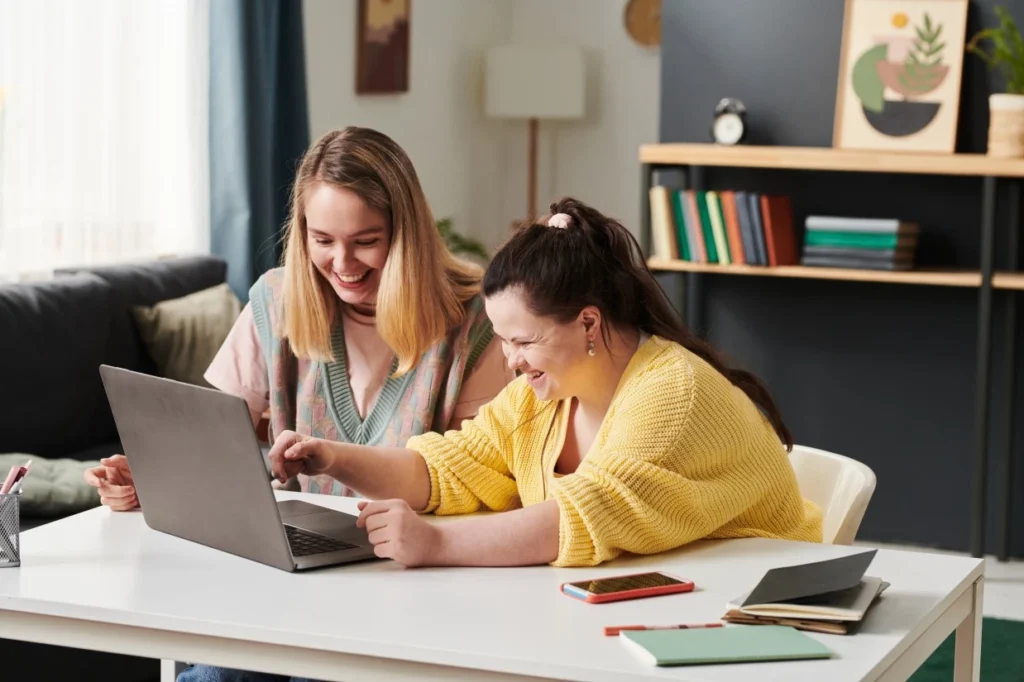 Girl with down syndrome laughing with carer in front of laptop