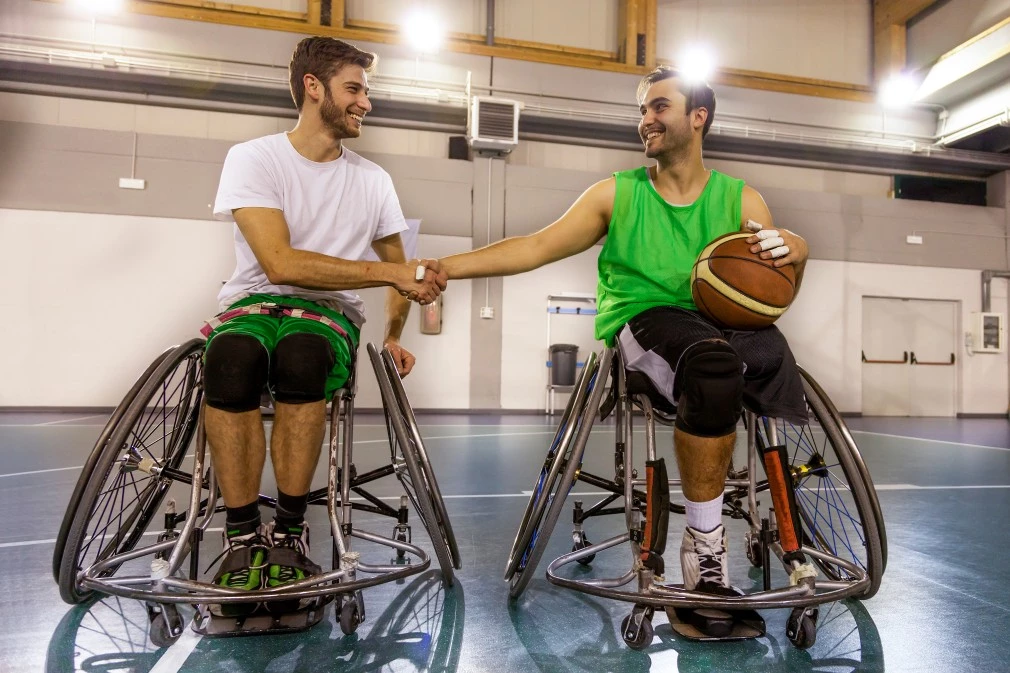 Two men in wheelchairs shaking hands after game of indoor basketball
