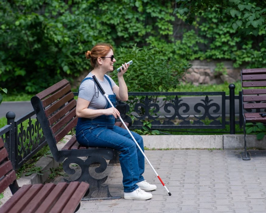 Blind woman sitting on park bench smiling while talking on phone