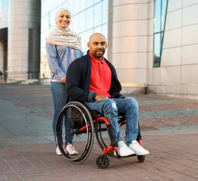 Man in wheelchair with Muslim support worker standing behind him smiling