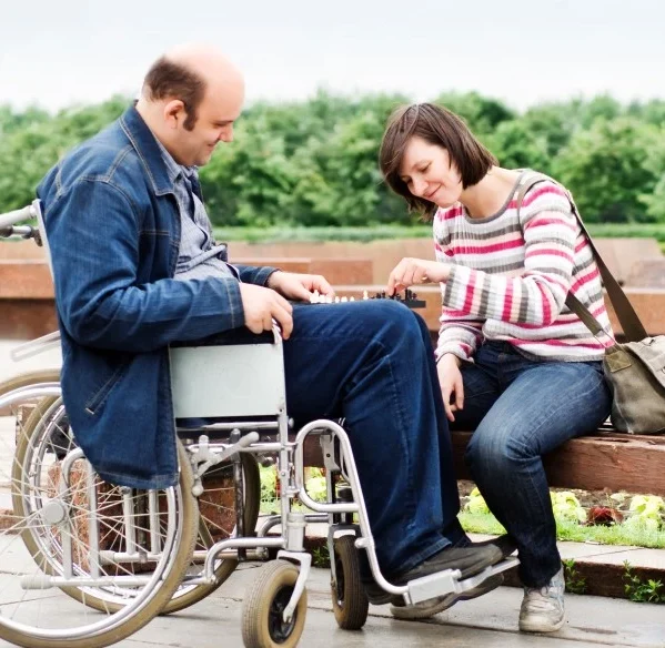 Disabled man in chair playing chess outside with support worker