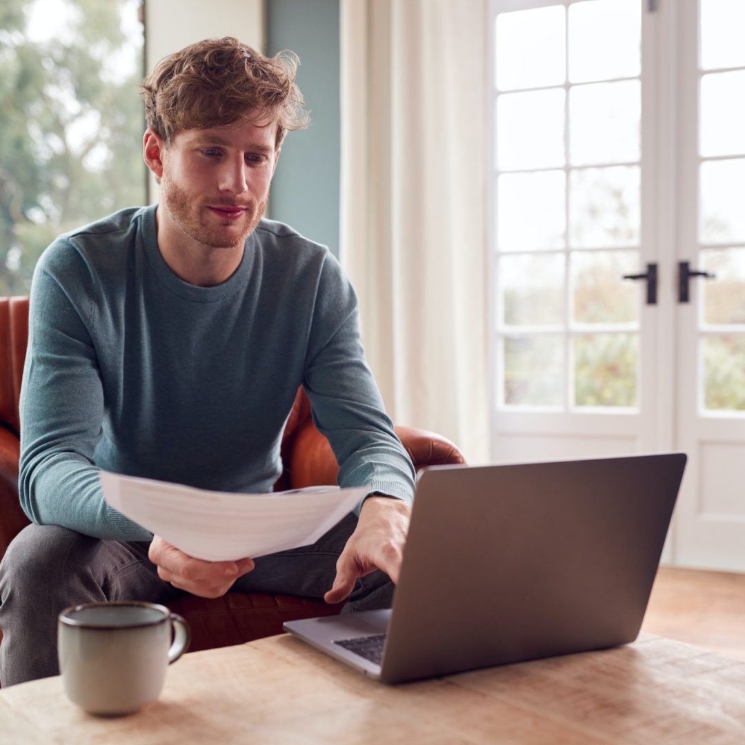 Man Sitting On Armchair At Home With Laptop